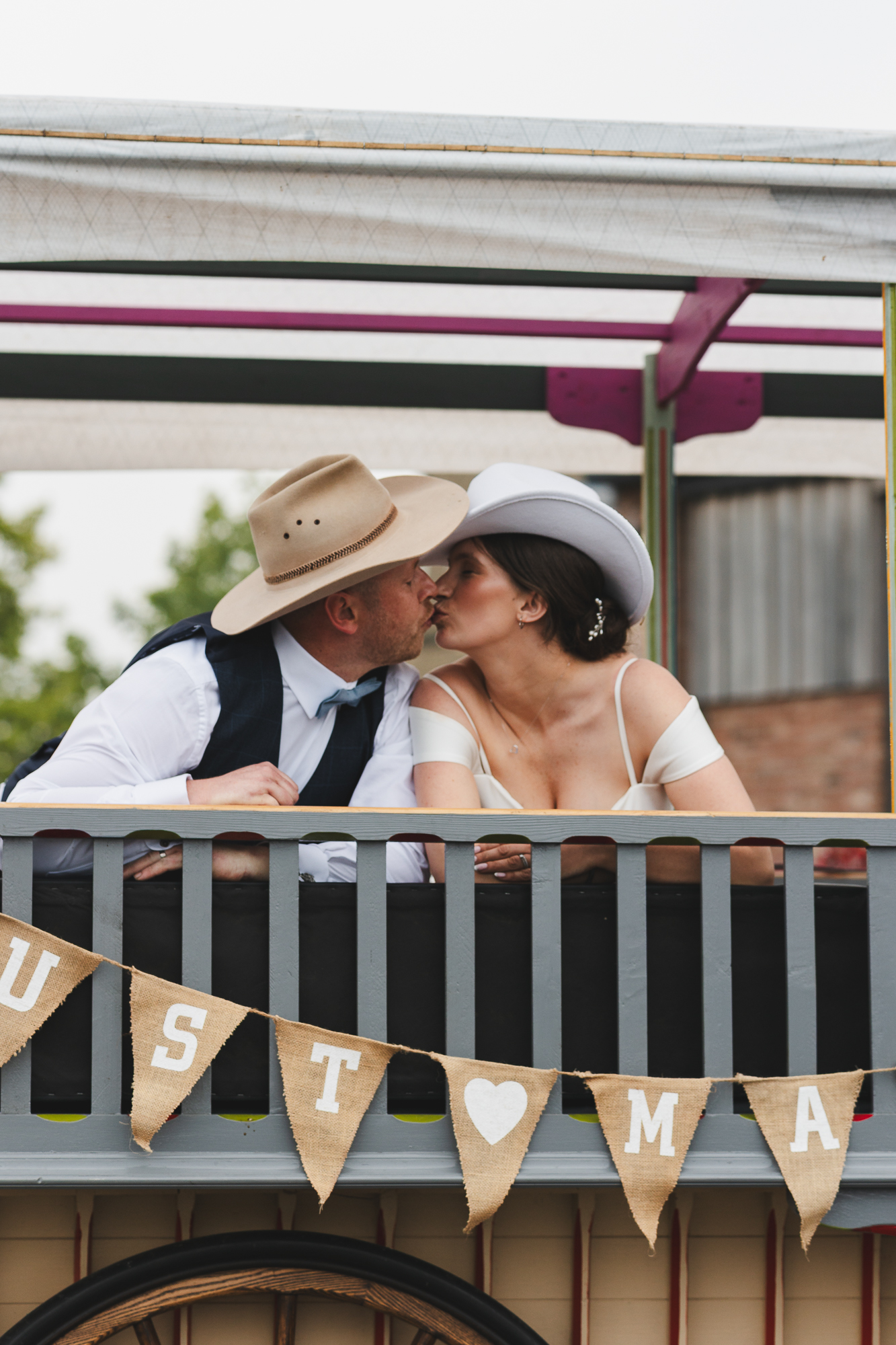 Bride and groom in cowboy hats sharing a kiss during a rustic Yorkshire barn wedding.